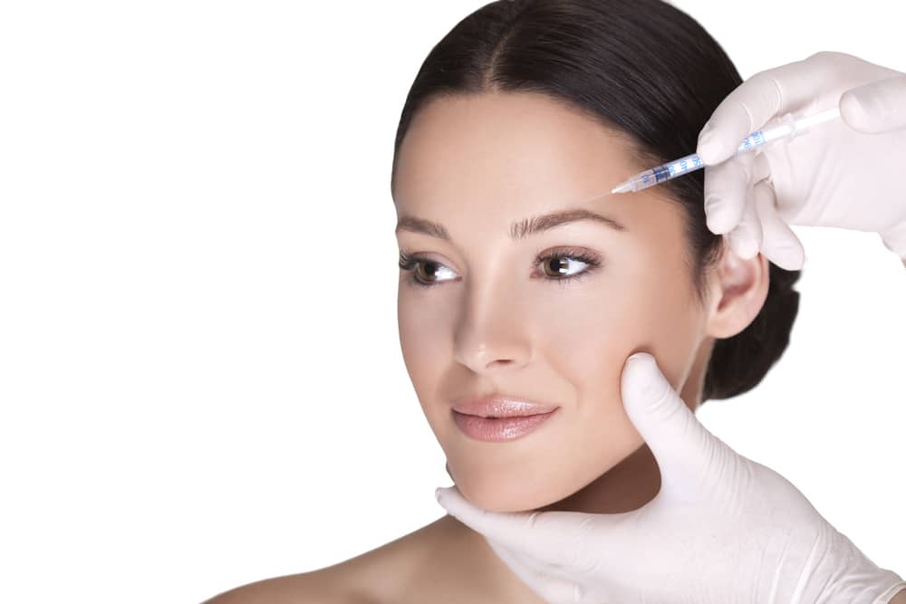 Woman with dark hair looks to the side as her medical provider injects Botox in her forehead