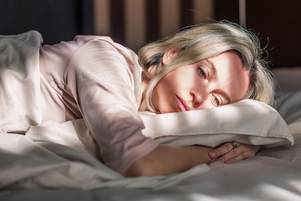 Woman, lying in bed, looks sad due to low libido before her female PRP intimacy shot