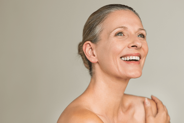 A smiling middle aged woman with blue eyes and light skin, looking off to the side.