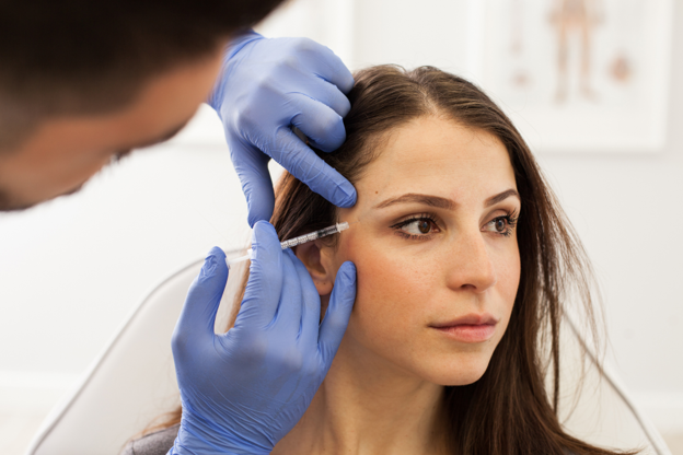 A woman receives a Botox injection near her eye from a medical professional wearing blue gloves in a clinical setting A woman receives a Botox injection near her eye from a medical professional wearing blue gloves in a clinical setting