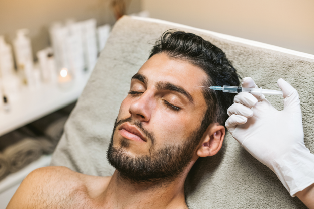 Man receiving a Botox injection near his temple from a medical professional wearing gloves in a clinical setting